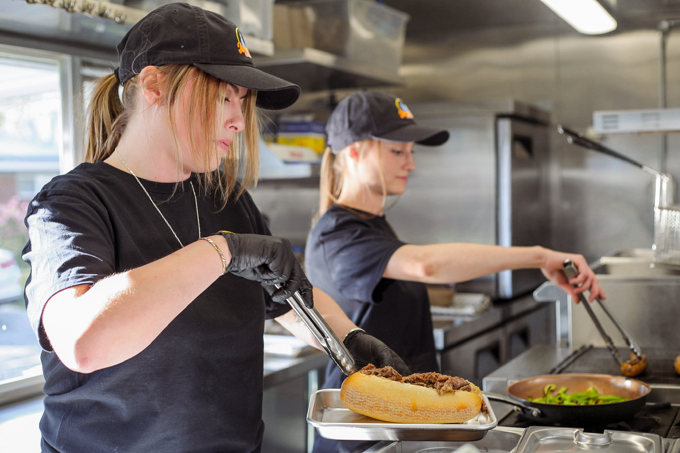 Two team members plating Italian beef sandwiches in the truck's kitchen