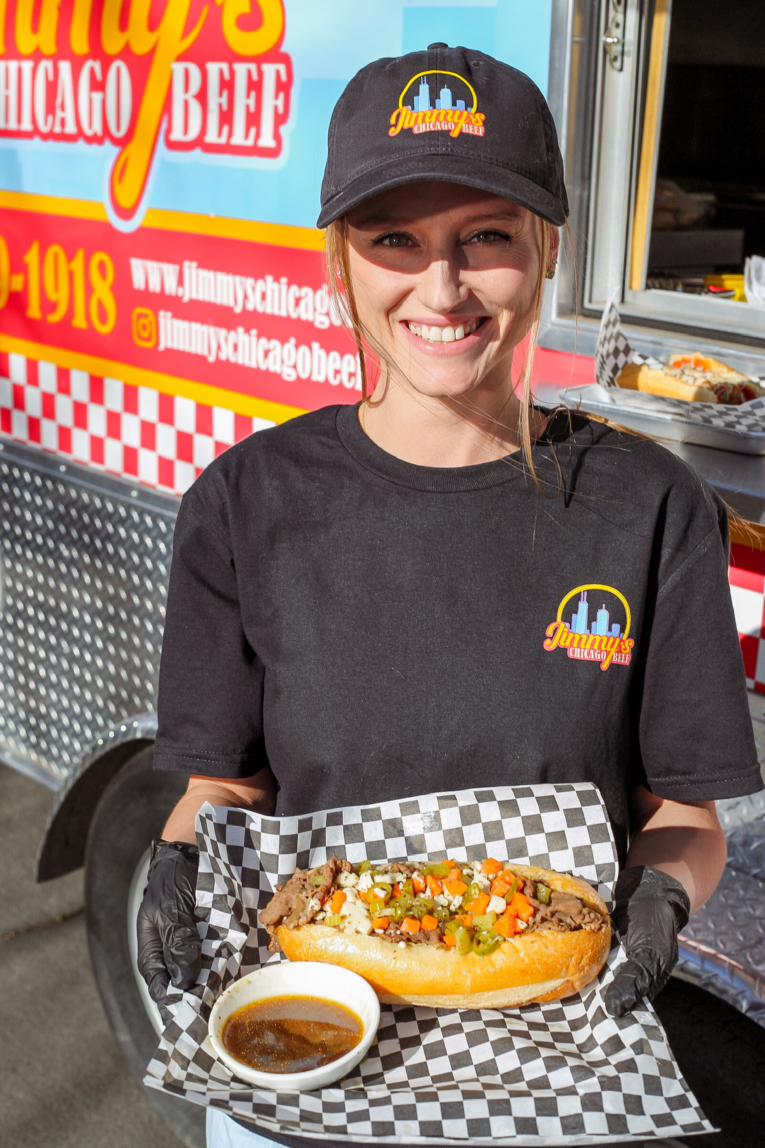 One of the Zukowski sisters smiling in front of the food truck, holding a fresh Italian beef sandwich